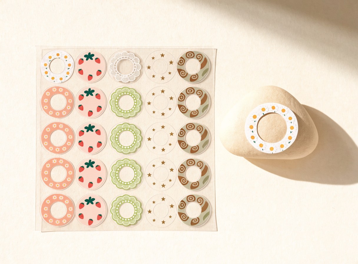 A sheet of hydrogel ring stickers in daisy, strawberry, lace, star and cinnamon prints, with a cream node wearing the daisy ring